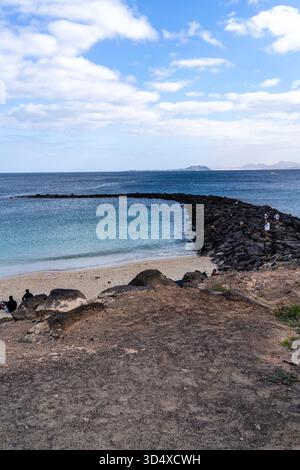 Eine malerische Aussicht auf Lanzarote mit einem Steinbruch, klarem blauem Wasser, einem Sandstrand und einem bewölkten Himmel. Stockfoto