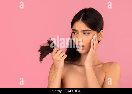 Junge Frau mit langen Haaren, die trockenes Haar untersucht, endet mit besorgtem Ausdruck Stockfoto