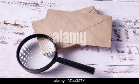 Korrespondenz im Blick: Lupenglas und Stapel brauner Umschläge auf Holz Stockfoto