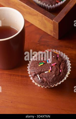 Schokoladenmuffin mit einer Tasse heißen Kaffee oder Tee auf rotbrauner Holztischoberfläche, weiche Fokussierung mit Kopierraum für Text, gemütliche Pause Stockfoto
