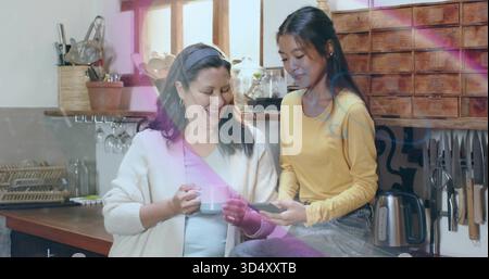 Die Tochter in Gelb auf der Theke und die Mutter in der Küche zu Hause, mit Telefon, Becher Stockfoto