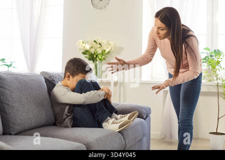 Wütende, emotionale Mutter schimpfend verärgerter Junge, der während eines Familienkonflikts zu Hause auf dem Sofa sitzt. Stockfoto