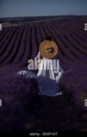 Lavendel, Frau, Feld, Spaziergang durch ein riesiges lila Lavendelfeld in einem weißen Kleid und Strohhut, genießen Sie die friedliche Sommerlandschaft. Stockfoto