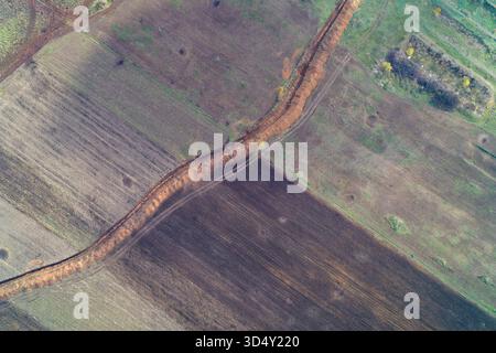 Luftbild mit einer Verteidigungslinie, die sich in Herbstfarben durch landwirtschaftliche Felder schlängelt und kontrastierende Strukturen von Boden, Gras und Ackerland von oben zeigt Stockfoto