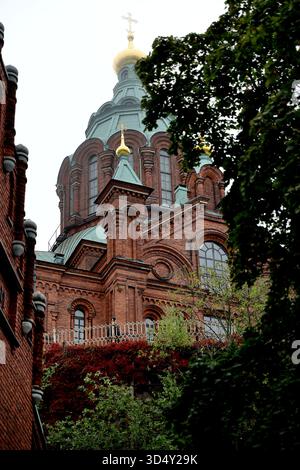 Detail der Uspenski Kathedrale mit Ziegelbögen, grünen Kupferdächern und goldenen Zwiebelkuppeln in Helsinki, Finnland, durch Blätter im Küstennebel gesehen. Stockfoto