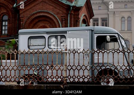 Seitenansicht eines Vintage-Van neben der Backsteinfassade der Kathedrale von Uspenski in Helsinki, Finnland, hinter einem eisernen Zaun an einem nebeligen Tag in der Stadt gesehen. Stockfoto