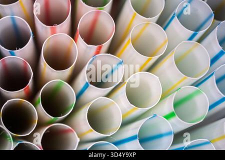 Nahaufnahme weißer, lichtdurchlässiger Trinkhalme mit farbigen Streifen in Rot, Gelb, Blau und Grün, die ihre kreisförmigen Öffnungen hervorheben. Stockfoto