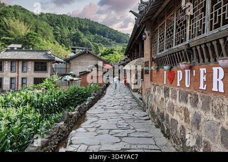 Blick auf den alten Steinweg schlängelt sich durch eine lebendige chinesische Stadt, wo traditionelle Architektur auf üppiges Grün unter einem ruhigen Himmel trifft, Nakeli, Chi Stockfoto