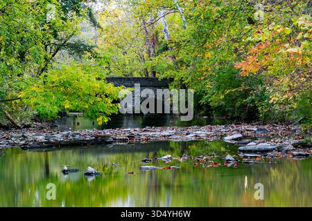 Blick auf eine Steinbrücke, die sich im stillen Wasser spiegelt, umgeben von den lebhaften Herbstfarben in Sharonville, Ohio, USA. Stockfoto