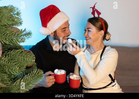 Ein Paar teilt sich während der Weihnachtszeit Marshmallows und heiße Schokolade in Tassen Stockfoto