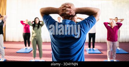 Trainer führt eine vielfältige Gruppe von Menschen während eines Fitnesstrainings mit Dehnungsübungen auf Matten in einem hellen Wellnesscenter Stockfoto