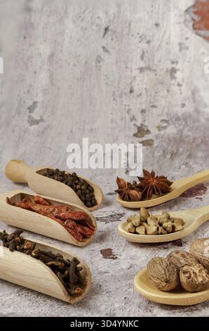Verschiedene aromatische getrocknete Gewürze und Kräuter in Holzlöffeln und Löffeln auf rustikalem Hintergrund, Kochzutaten und Gewürze Stockfoto