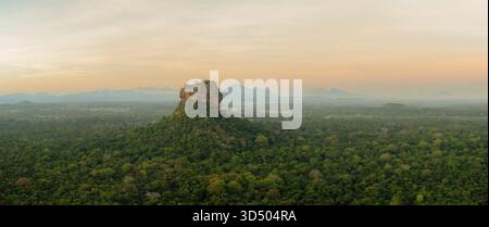 Ein breiter Panoramablick aus der Luft fängt den majestätischen Sigiriya (Löwenfelsen) ein, der sich dramatisch aus dem dichten, flachen Dschungel der cultura von Sri Lanka erhebt Stockfoto
