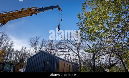 Der Ausleger eines LKW-Krans hebt das modulare Haus an, damit es zur vorbereiteten Baustelle transportiert werden kann. Stockfoto