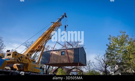 Das modulare Haus wird vom Ausleger des LKW-Krans angehoben und zum vorgesehenen Standort transportiert. Stockfoto