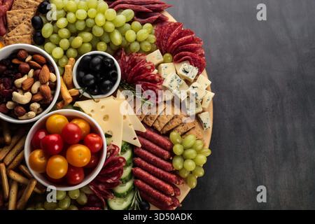 Eine große Holzplatte ist gefüllt mit verschiedenen Fleischsorten, Käse und frischem Obst. Es gibt Trauben, Kirschtomaten und Oliven sowie Cracker und Stockfoto