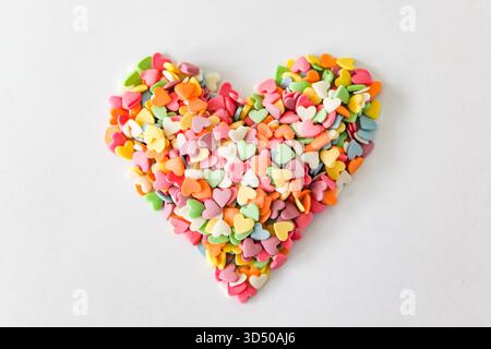 Bunte herzförmige Süßigkeiten werden sorgfältig angeordnet, um ein Herz auf einem schlichten weißen Hintergrund zu bilden. Diese Dekoration ist perfekt für Feiern, Stockfoto