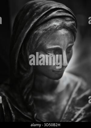 Schwarz-Weiß-Nahaufnahme einer Grabstatue einer verschleierten Frau mit gesenktem Kopf und zartem Gesicht auf dem Friedhof Kozia brana in Bratislava, Slowakei. Stockfoto