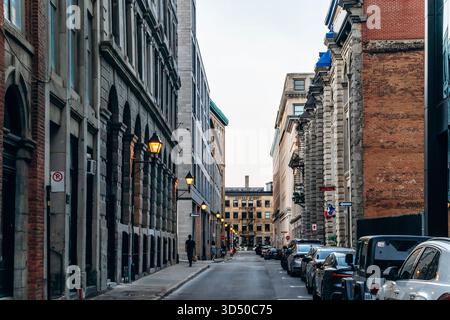 Montreal, Kanada - 11. August 2025: Abendliche Stadtlandschaft mit historischem Lovell und Son Gebäude, Vintage Straßenlaternen, Autos und Menschen in der Rue le Moyne in Stockfoto