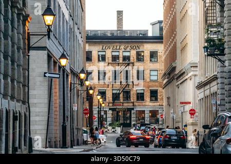 Montreal, Kanada - 11. August 2025: Abendliche Stadtlandschaft mit historischem Lovell und Son Gebäude, Vintage Straßenlaternen, Autos und Menschen in der Rue le Moyne in Stockfoto