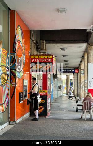 Haifa, Israel, 4. November 2025, Ein Mann in traditioneller, ultraorthodoxer jüdischer Kleidung, der einen geldautomaten an einem kleinen Street-Food-Stand im Freien betreibt Stockfoto