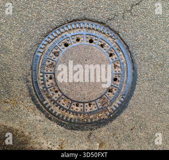Bordesholm, Deutschland - 08. November 2025: Runde gusseiserne Mannlochabdeckung auf Asphaltpflaster. Zugang zur Versorgungsleitung für Abfluss-, Wasser- oder Kanalsysteme in der c Stockfoto