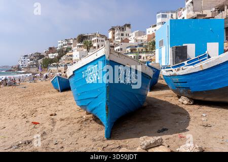 Traditionelle blaue Fischerboote ruhen am Sandstrand des lebendigen Fischerdorfes Taghazout, Marokko, entlang der Atlantikküste Stockfoto