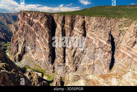 Blick auf die massive Painted Wall im Black Canyon des Gunnison National Park. Weiße Pegmatitdeiche bilden Streifen auf der dunklen, transparenten Klippe. Der Gunnison River ist unten sichtbar Stockfoto