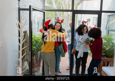 Verschiedene Freunde umarmen und tauschen Geschenkboxen mit Weihnachtsmützen im modernen Kopierraum für den Hauseingang aus Stockfoto
