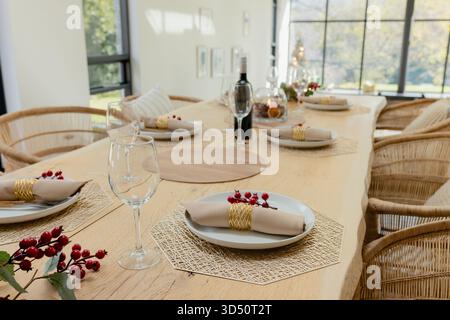 Esstisch aus rustikalem Holz mit gewebten Tischsets, Tellern und Weingläsern im Licht des Fensters Stockfoto
