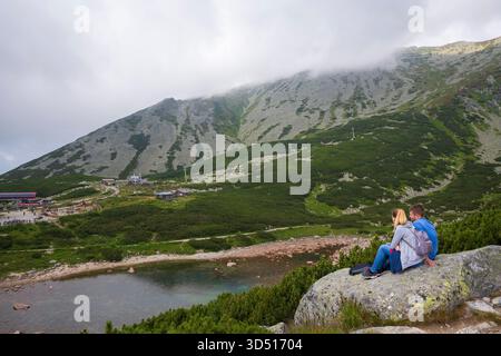 Ein Paar sitzt auf einem Felsen neben Skalnaté Pleso, einem wunderschönen Bergsee in der hohen Tatra. Stockfoto