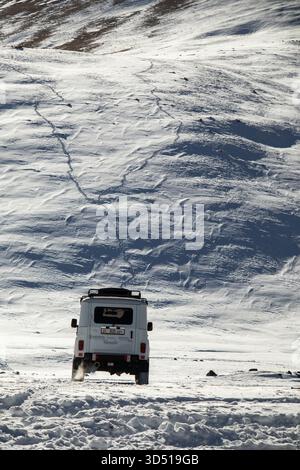 Naryn, Kirgisistan - 12. November 2025: Die Rückansicht eines weißen UAZ Patriot 4x4, der durch eine verschneite Ebene fährt, mit sichtbaren Spuren, die den V hinaufführen Stockfoto