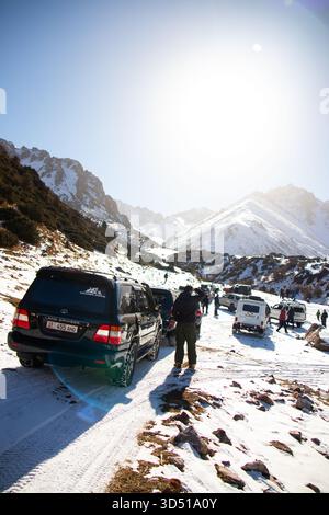 Naryn, Kirgisistan – 12. November 2025: Ein Konvoi von Geländefahrzeugen, geführt von einem schwarzen Toyota Land Cruiser, parkte auf einer verschneiten Strecke mit mehreren Erwachsenen Stockfoto