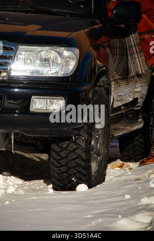 Naryn, Kirgisistan – 12. November 2025: Nahaufnahme der vorderen Ecke, des Scheinwerfers und des Geländebereifens eines schwarzen Toyota Land Cruiser 100, Park Stockfoto