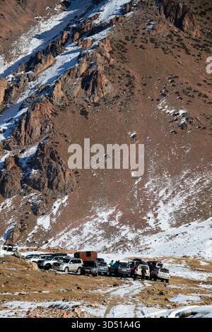 Naryn, Kirgisistan - 12. November 2025: Eine enge Gruppe von Geländewagen und Geländewagen versammelte sich am Fuße eines steilen, trockenen Berghanges, der von Schnee bedeckt war Stockfoto