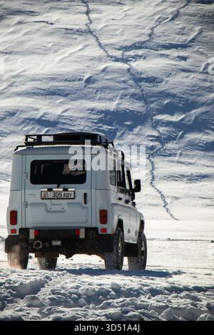 Naryn, Kirgisistan - 12. November 2025: Rückansicht eines weißen UAZ Patriot 4x4, der auf einer verschneiten Strecke in Richtung eines riesigen, strukturierten, schneebedeckten mou fährt Stockfoto