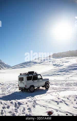 Naryn, Kirgisistan - 12. November 2025: Ein weißer UAZ Patriot 4x4 fährt auf einer breiten, schneebedeckten Ebene, umgeben von Bergen unter einem hellen, sonnigen Himmel mit l Stockfoto