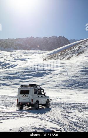 Naryn, Kirgisistan - 12. November 2025: Rückansicht eines weißen UAZ Patriot 4x4, der durch ein riesiges, strukturiertes, schneebedecktes Tal mit Bergen fährt Stockfoto