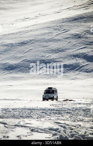Naryn, Kirgisistan - 12. November 2025: Die Rückansicht eines weißen UAZ Patriot 4x4, der durch eine verschneite Ebene fährt, mit sichtbaren Spuren, die den V hinaufführen Stockfoto