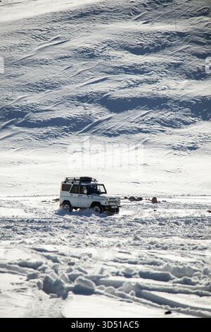 Naryn, Kirgisistan - 12. November 2025: Ein weißer UAZ Patriot 4x4 fährt über eine verschneite Ebene in Richtung Kamera, mit einem riesigen, strukturierten schneebedeckten Hügel Stockfoto