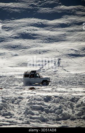 Naryn, Kirgisistan - 12. November 2025: Ein weißer UAZ Patriot 4x4 fährt über eine verschneite Ebene in Richtung Kamera, mit einem riesigen, strukturierten schneebedeckten Hügel Stockfoto