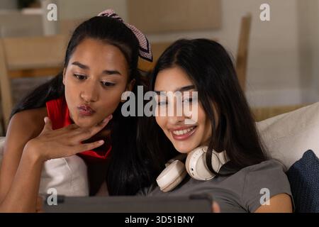 Mit über-Ohr-Kopfhörern können Sie verschiedene weibliche Freunde auf der Couch im Wohnzimmer anschauen Stockfoto