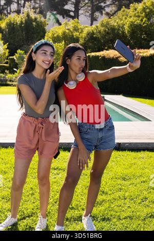 Mit Smartphone und Kopfhörern können verschiedene Freundinnen im privaten Garten Selfie machen Stockfoto