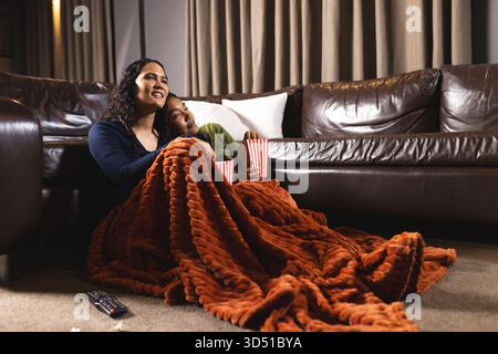 Afroamerikaner-Mutter und -Tochter auf dem Boden im Wohnzimmer sitzen zu sehen, mit Popcornbechern Stockfoto