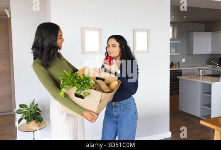 Verschiedene weibliche Freunde halten eine Lebensmittelbox und riechen drinnen roten Paprika mit Topfpflanzen Stockfoto