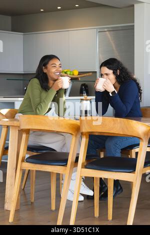 Sie unterhalten sich mit verschiedenen Freundinnen beim Kaffeetrinken in einer modernen Küchenecke, mit französischer Presse und Tassen Stockfoto
