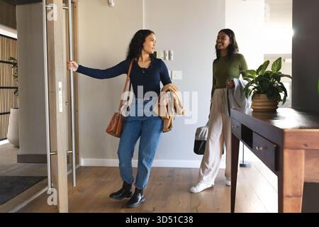 Verschiedene Freundinnen betreten das Foyer durch eine Holztür mit Taschen und Jacken Stockfoto