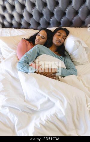 Ein weibliches Paar mit Löffeln kuschelt unter weißer Bettdecke im Schlafzimmer mit getuftetem Lederkopfteil Stockfoto