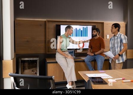 Zusammenarbeit mit verschiedenen Kollegen, die Daten in modernen Konferenzbereichen mit einem wandmontierten Bildschirm prüfen Stockfoto