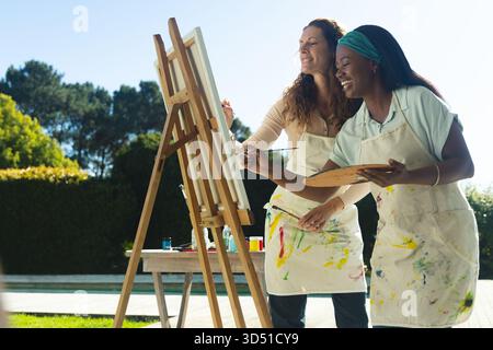 Ich malte verschiedene Freundinnen, die an der Staffelei auf der Terrasse zusammenarbeiten, mit Palette und Pinsel Stockfoto